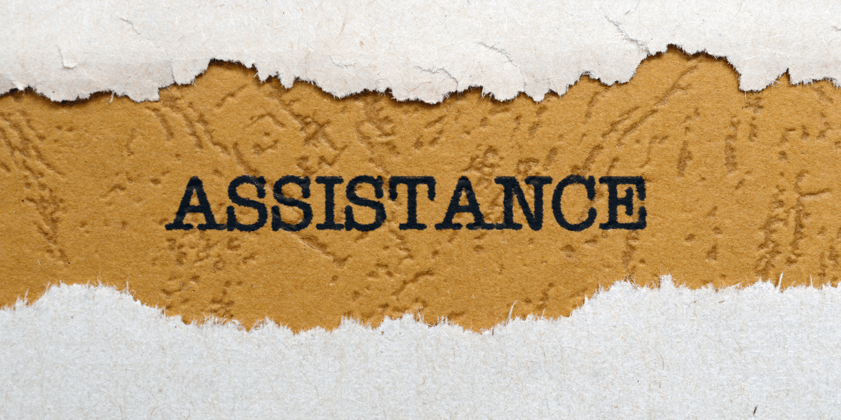 A corkboard with a torn sheet of paper revealing the word "assistance"